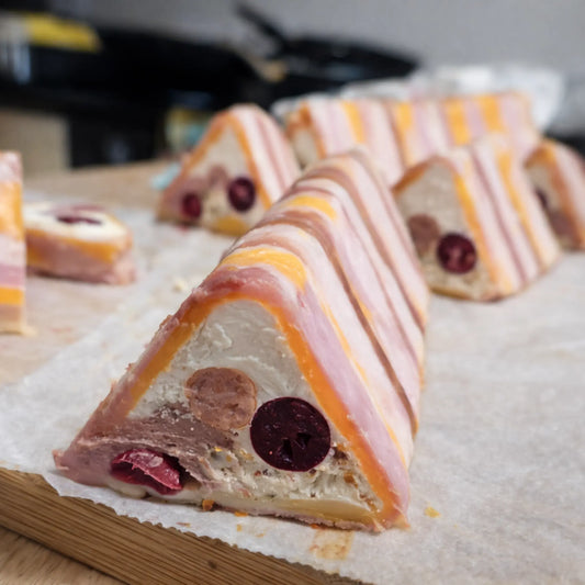 Triangular slices of layered charcuterie meat pâté on a wooden board, made using a professional stainless steel V-Shape terrine mold