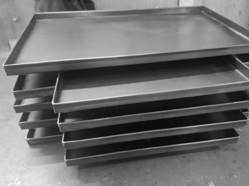 Stacked black steel baking trays in workshop