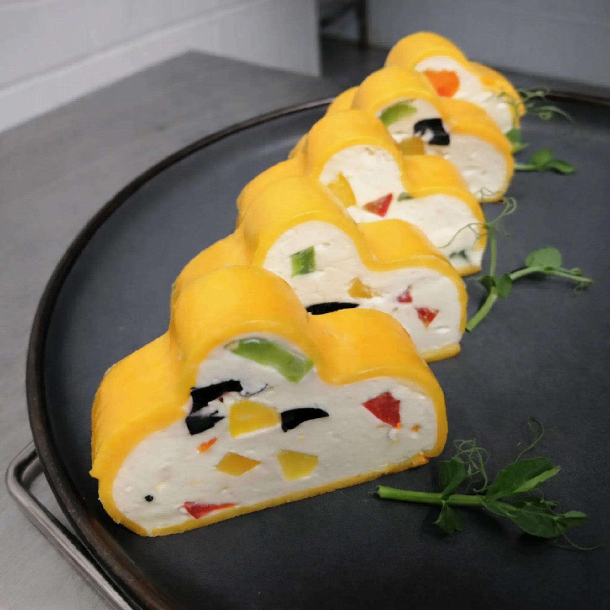 Sliced clover-shaped cheese and vegetable appetizers with a yellow coating on a dark plate, shaped using a professional stainless steel Clover Shape terrine mold