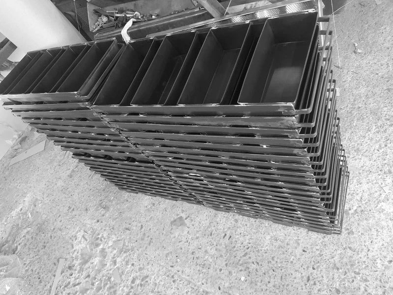 Stacks of heavy-duty black steel 4-strap bread loaf pans in a professional workshop, showcasing industrial-grade bakeware for commercial bakeries.
