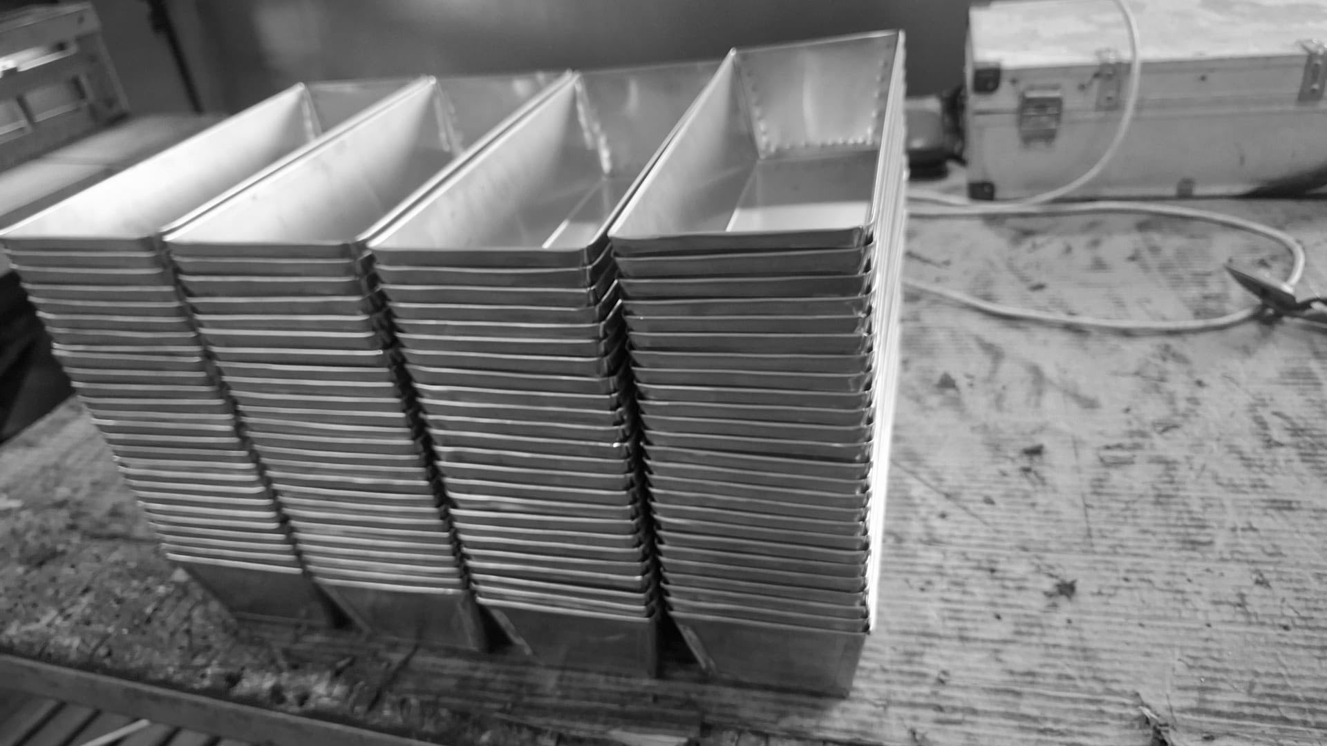 Stacks of commercial stainless steel bread molds on a factory workbench during the manufacturing process.