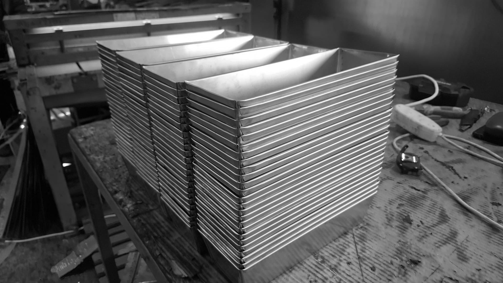 Heavy-duty stainless steel baking tins stacked on a workbench in our manufacturing facility.