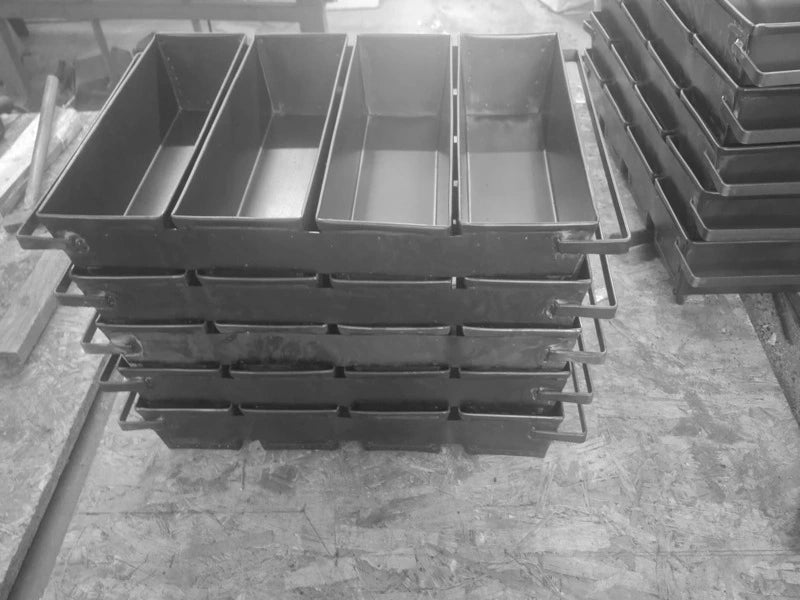 Close-up of a stacked professional 4-strap loaf pan set made of durable black steel, designed for high-volume commercial baking and optimal heat absorption.