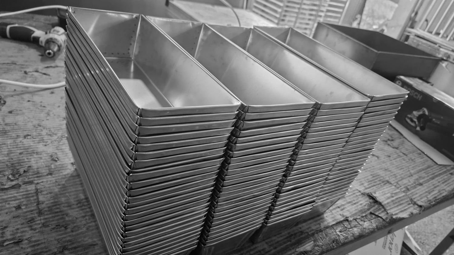 Large stack of freshly manufactured stainless steel loaf pans on a workshop table in our facility.